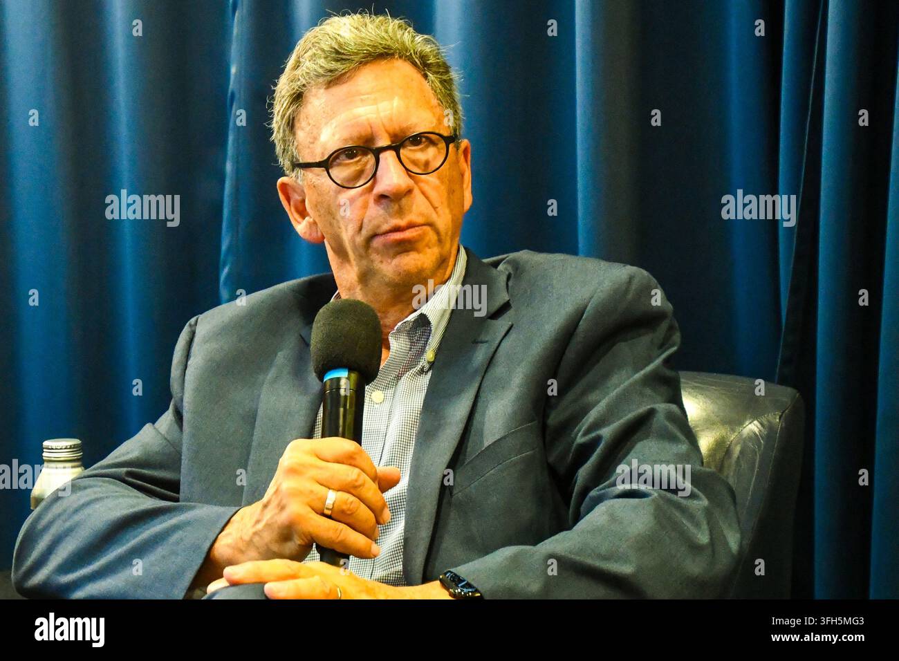 Frank Sesno seated and holding a microphone